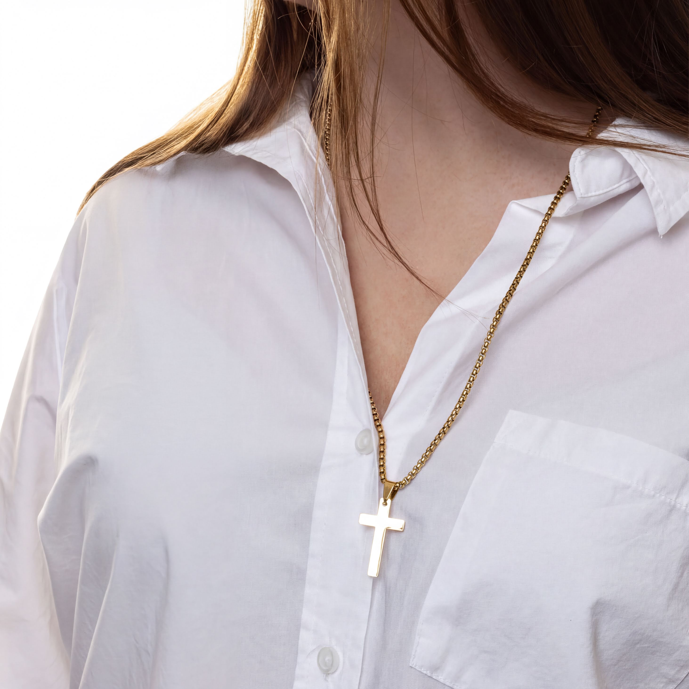 Gold necklace with a cross pendant worn by a person in a white shirt.