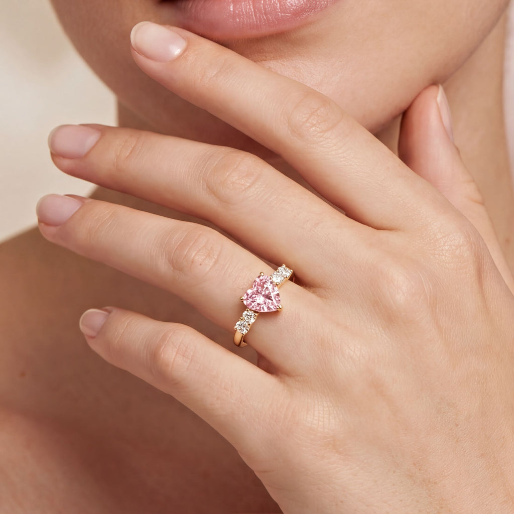 A close-up of a person's hand wearing a gold ring with a pink diamond.