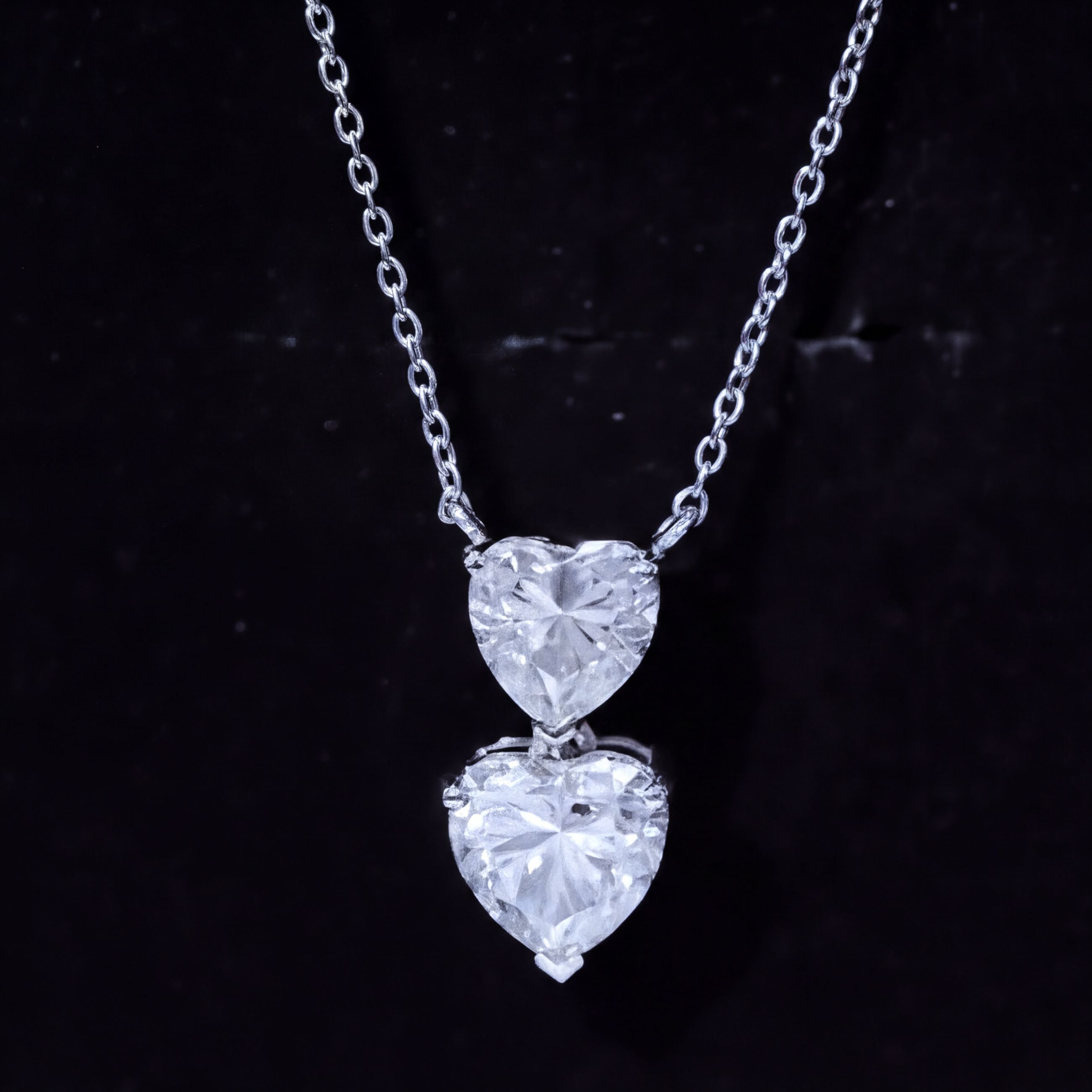 A necklace with a pendant featuring two large, clear diamonds set in a heart shape.