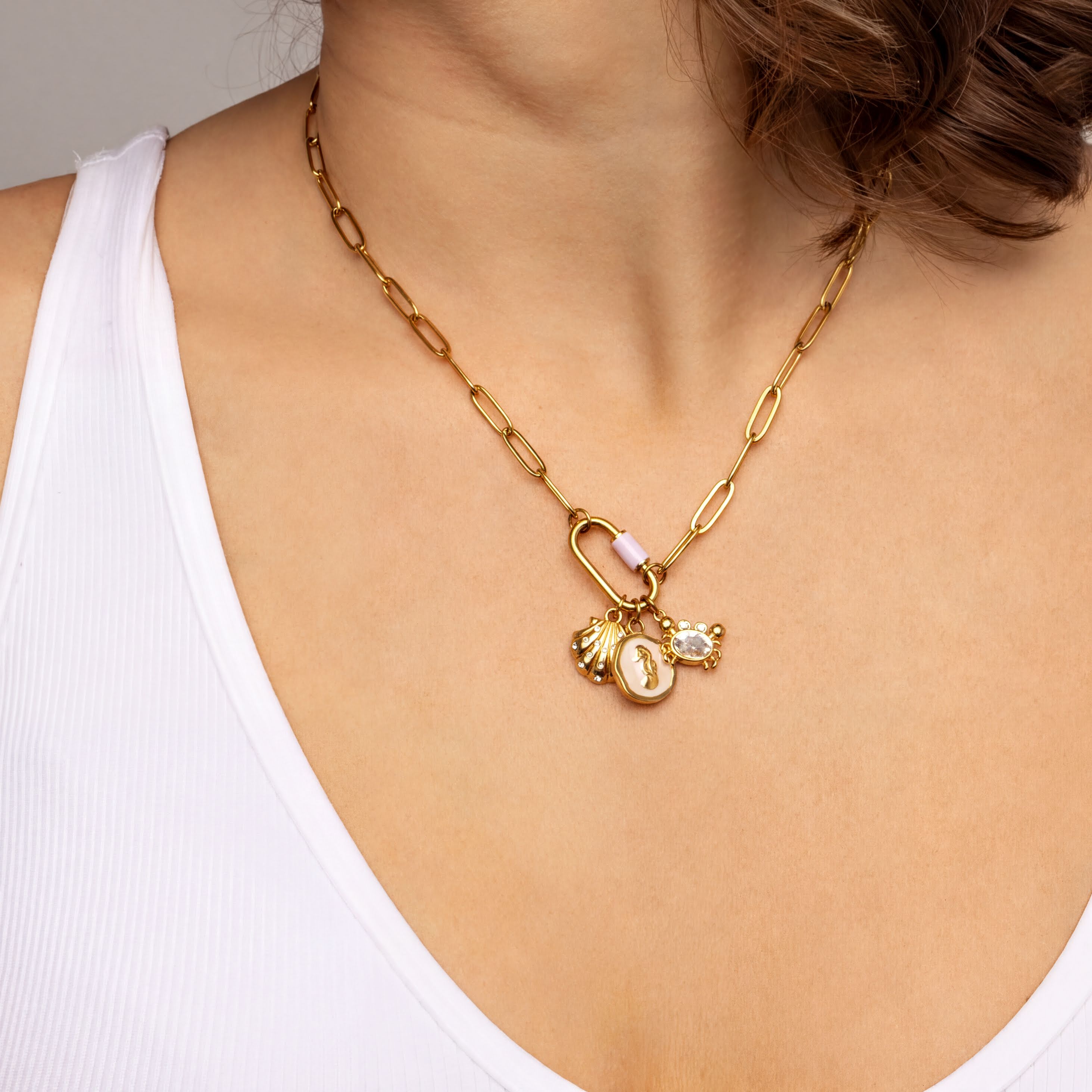 A close-up view of a woman's neck and chest area wearing a gold chain necklace with a pendant and charms.
