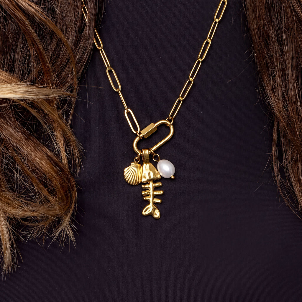 A gold necklace with a pendant featuring a fish design and a pearl.