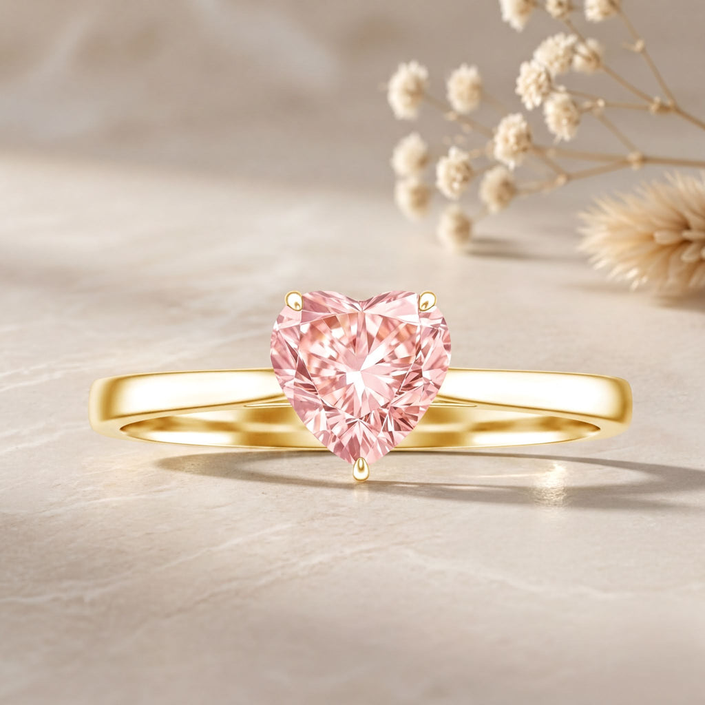 A gold ring with a pink diamond in the center, placed on a light-colored surface.