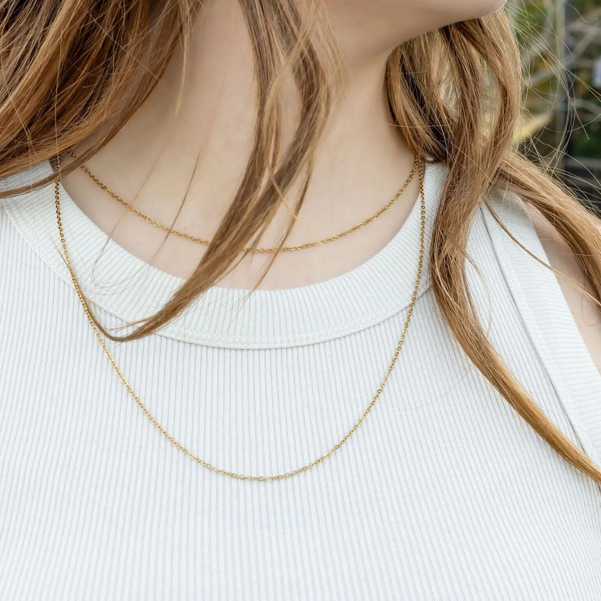 Person wearing a delicate gold necklace with a blurred background