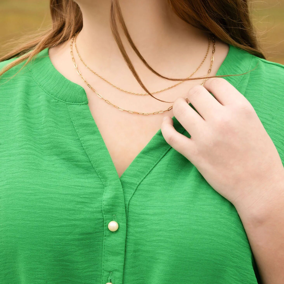 Person wearing a green top with a gold necklace and hand adjusting the neckline.
