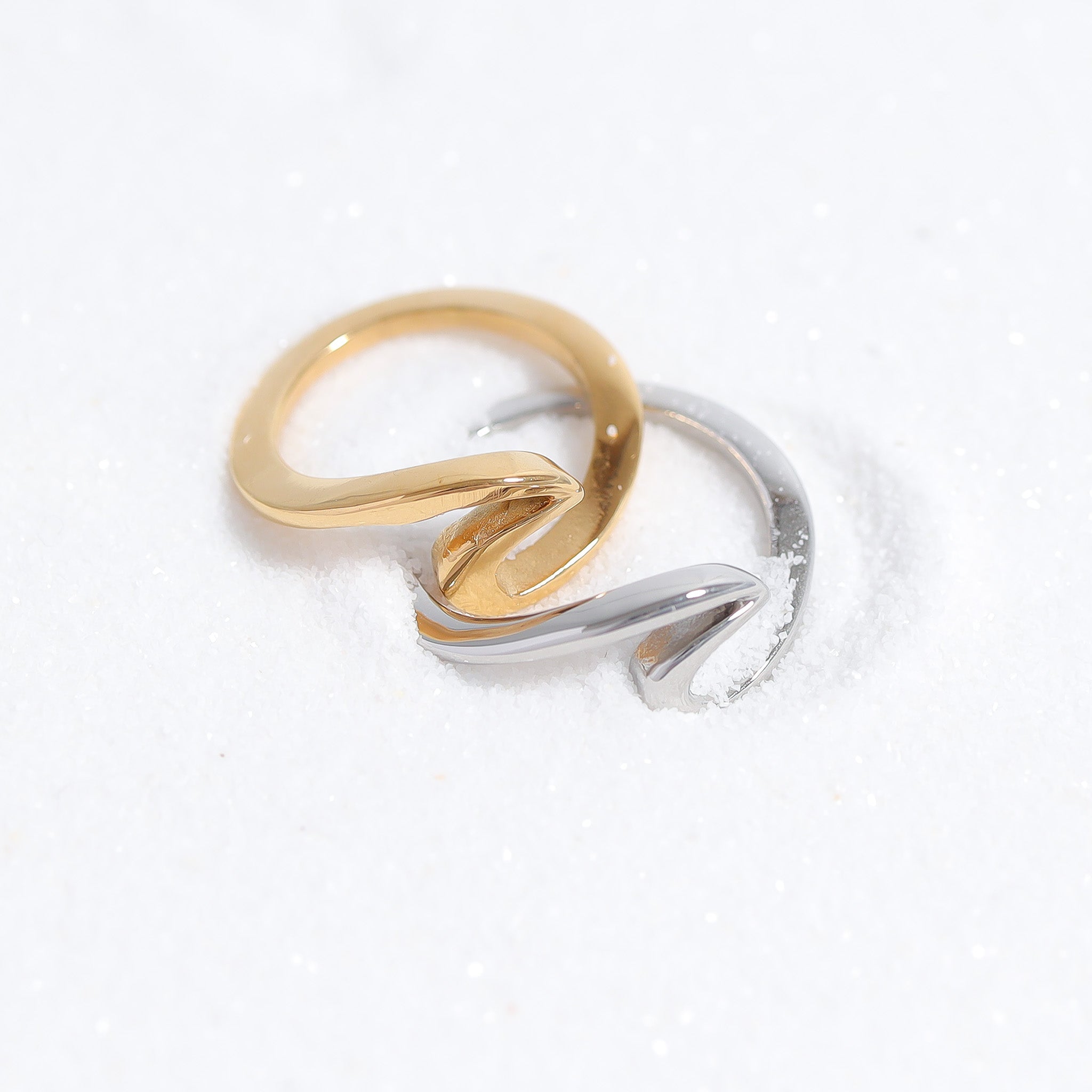 Two rings, one gold and one silver, are lying on a snowy surface.
